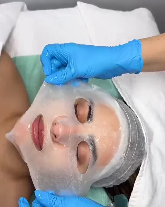 A sheet mask being smoothed onto a client's face in Jiman's treatment room